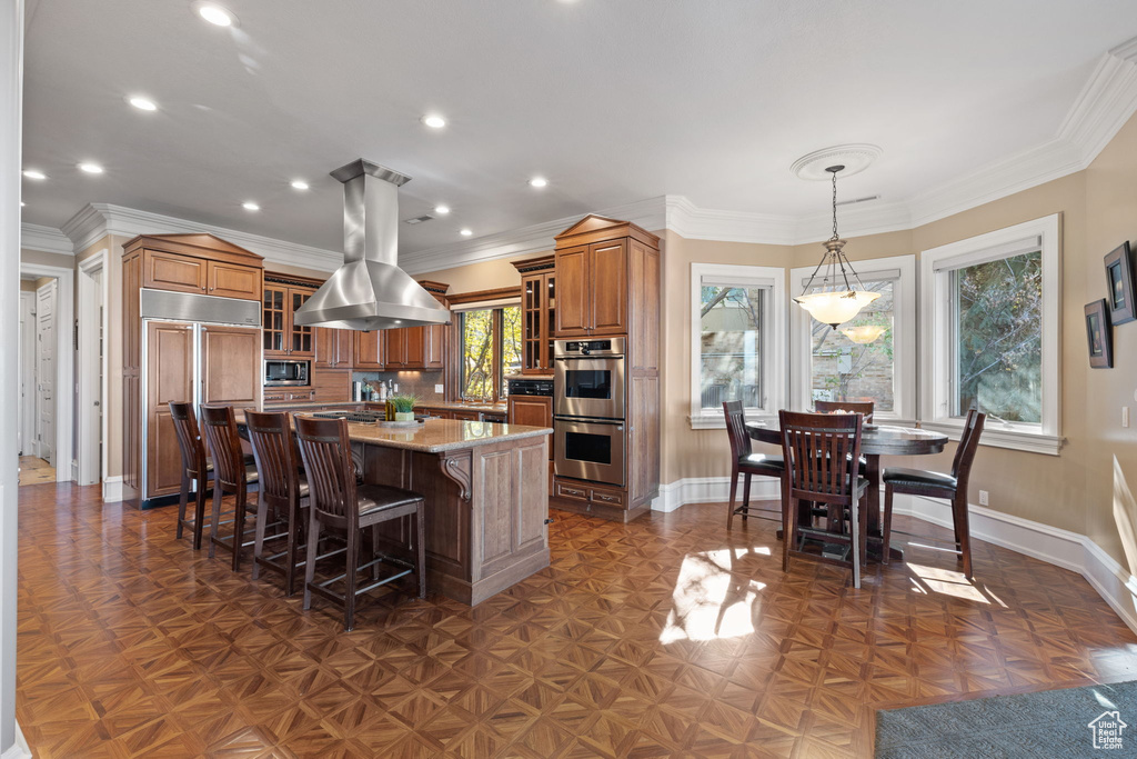 Kitchen featuring built in appliances, a wealth of natural light, island exhaust hood, and a kitchen island