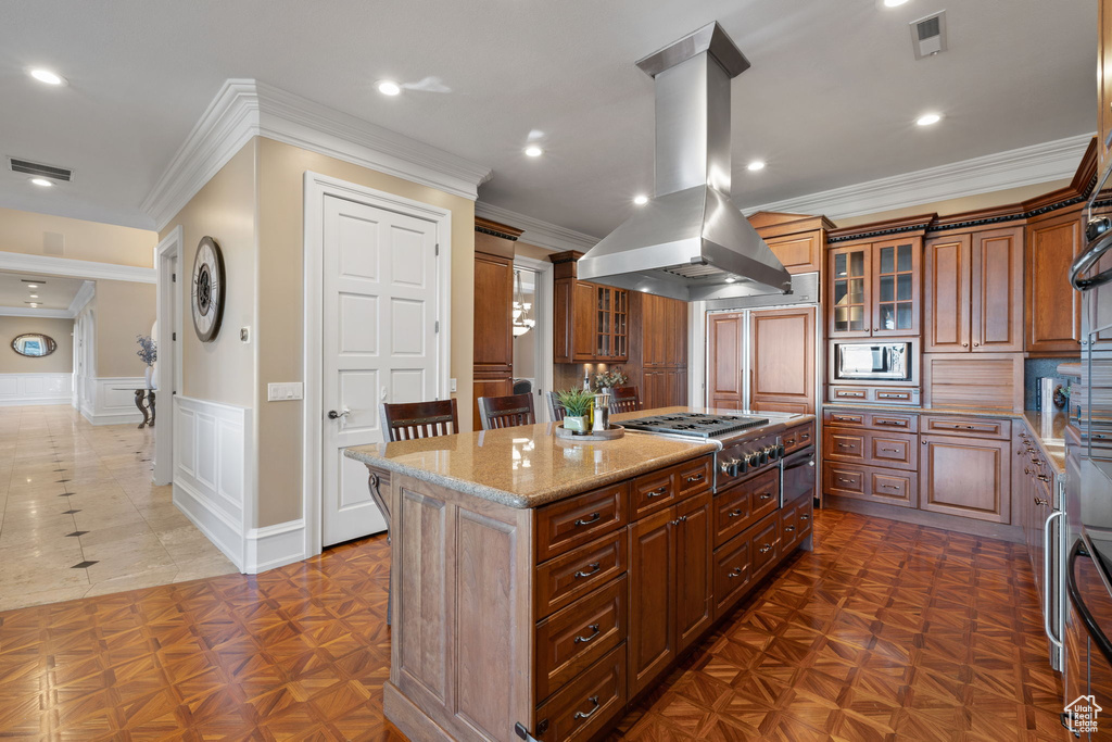 Kitchen featuring light stone countertops, crown molding, island exhaust hood, a kitchen island, and appliances with stainless steel finishes