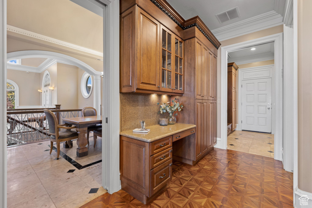 Interior space with dark parquet floors, decorative backsplash, light stone counters, and crown molding