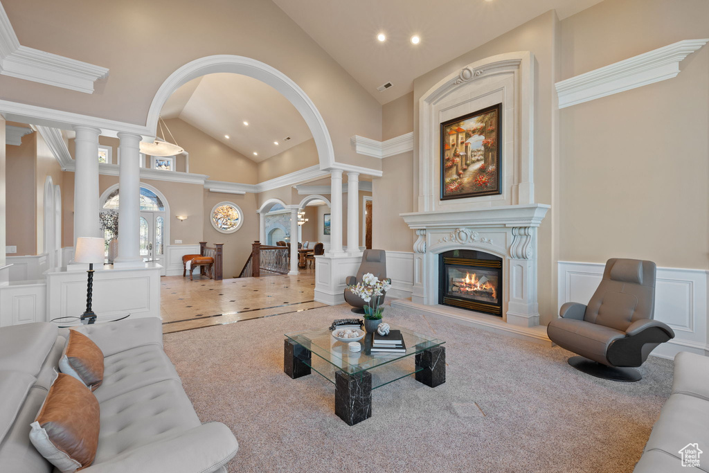 Carpeted living room featuring high vaulted ceiling, ornamental molding, and ornate columns