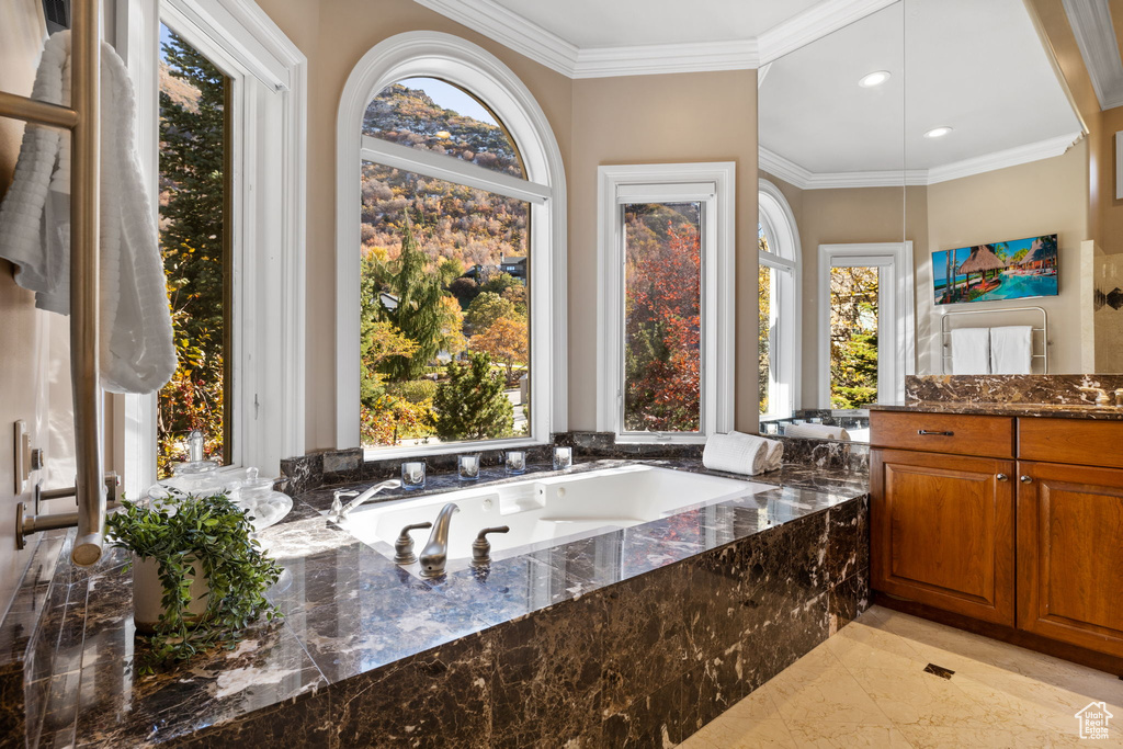 Bathroom featuring vanity, a relaxing tiled tub, and crown molding