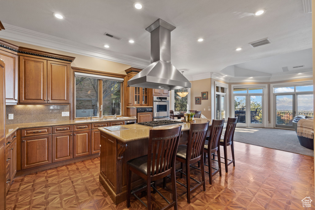 Kitchen featuring island range hood, tasteful backsplash, crown molding, light stone countertops, and a center island