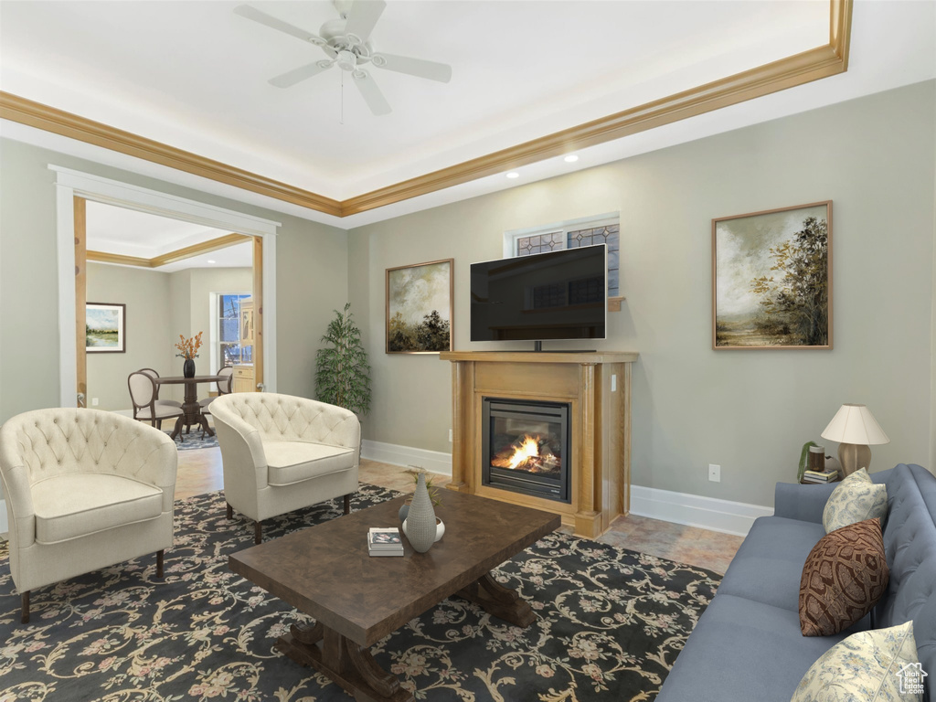 Living room featuring a raised ceiling, ornamental molding, a glass covered fireplace, ceiling fan, and baseboards