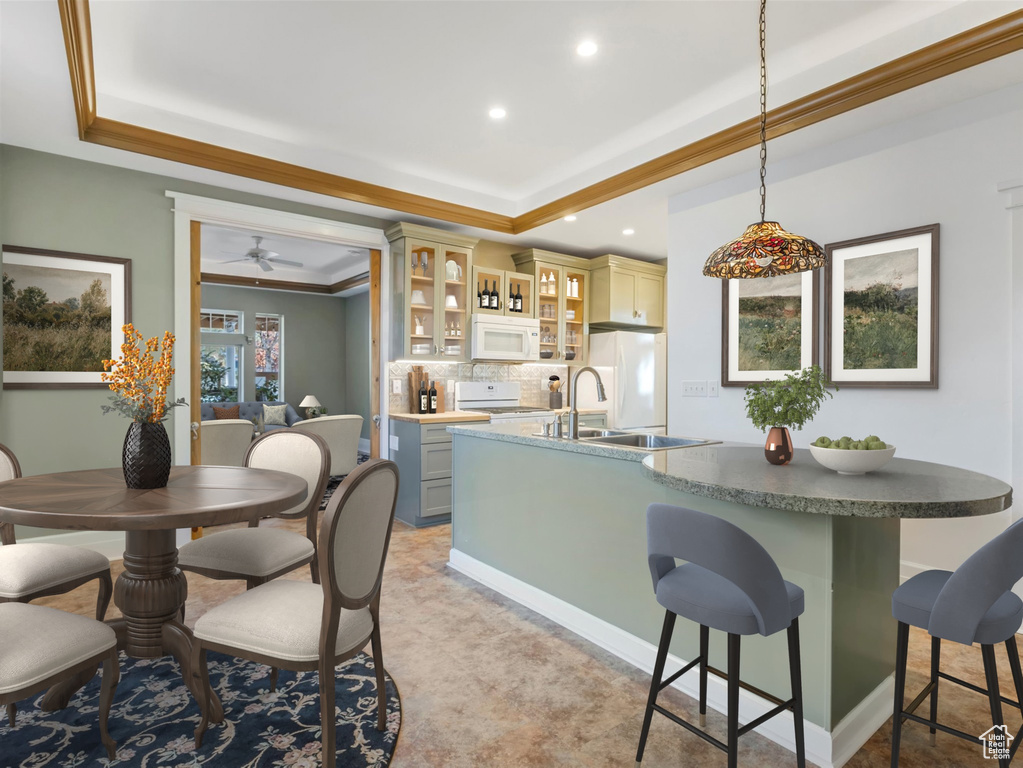 Kitchen with white appliances, a sink, backsplash, a raised ceiling, and a kitchen bar