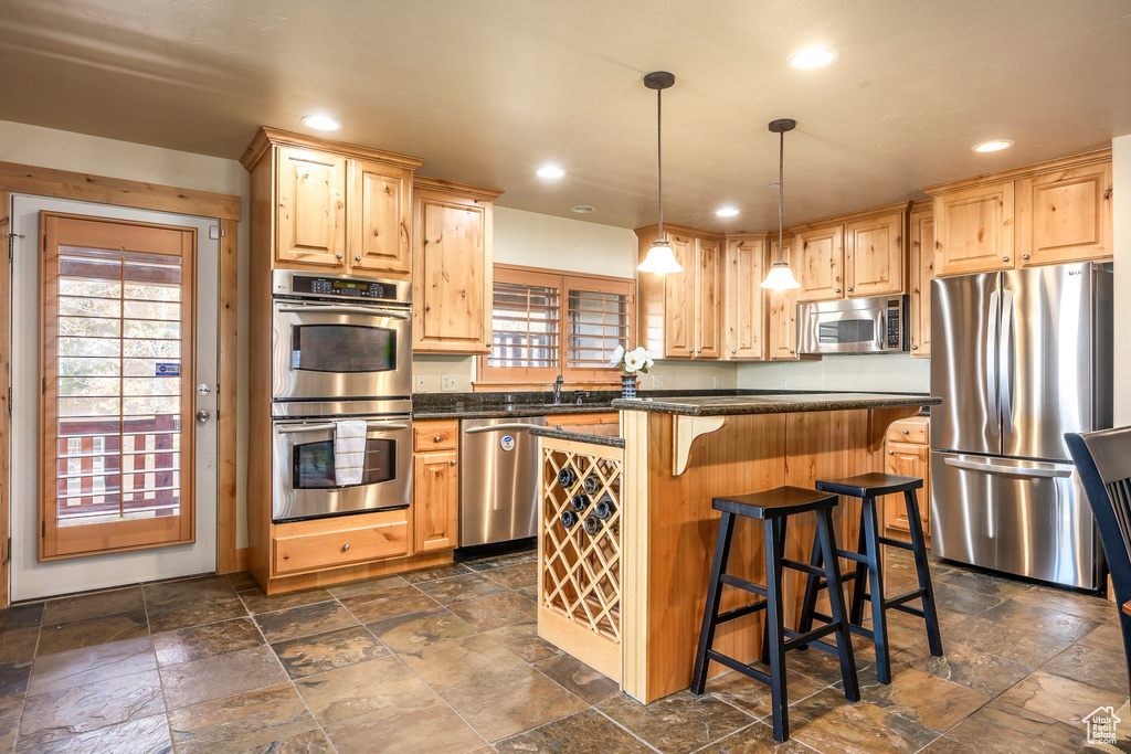 Kitchen featuring hanging light fixtures, a kitchen breakfast bar, a kitchen island, light brown cabinets, and appliances with stainless steel finishes