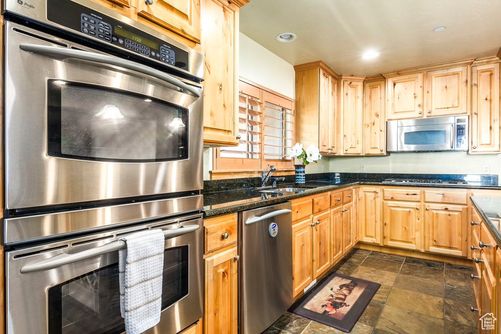 Kitchen featuring dark stone counters, light brown cabinets, appliances with stainless steel finishes, and sink