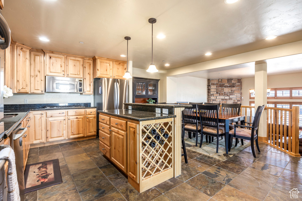 Kitchen with pendant lighting, stainless steel appliances, light brown cabinetry, and a kitchen island