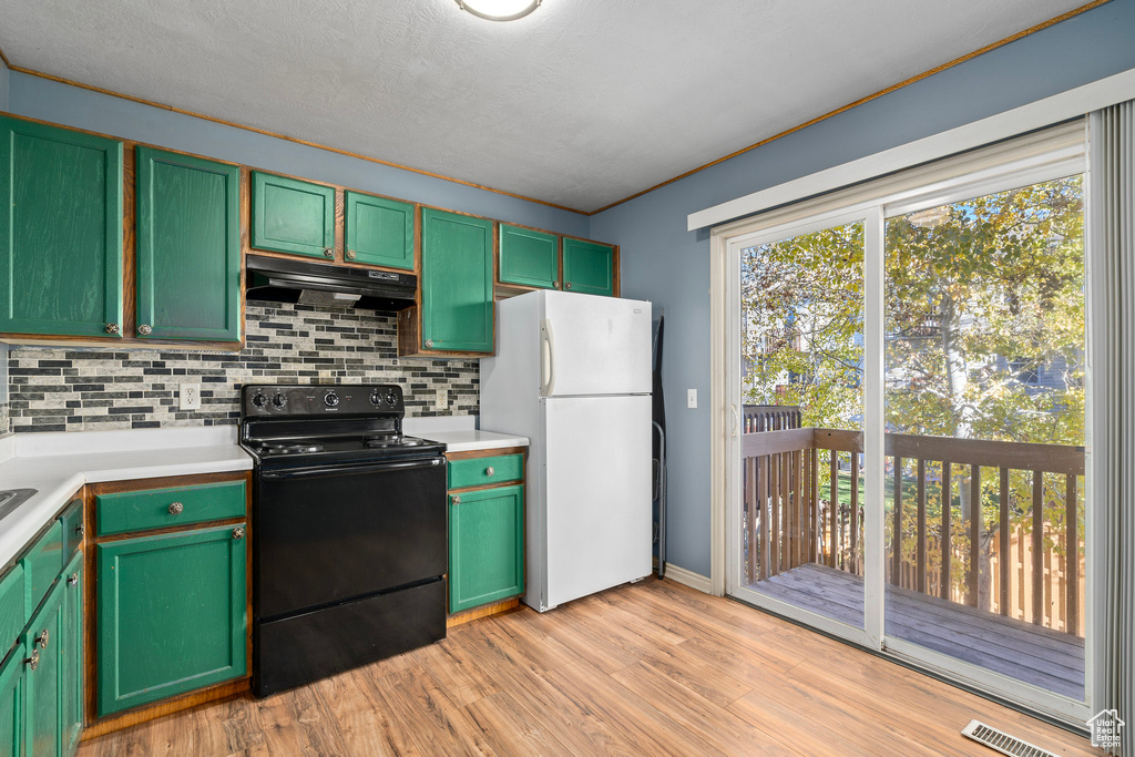 Kitchen with white refrigerator, green cabinets, black / electric stove, tasteful backsplash, and light wood-type flooring