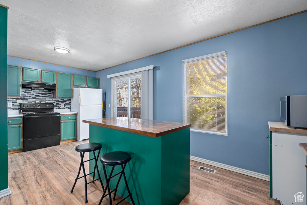 Kitchen featuring black range with electric cooktop, a wealth of natural light, a breakfast bar area, and white refrigerator