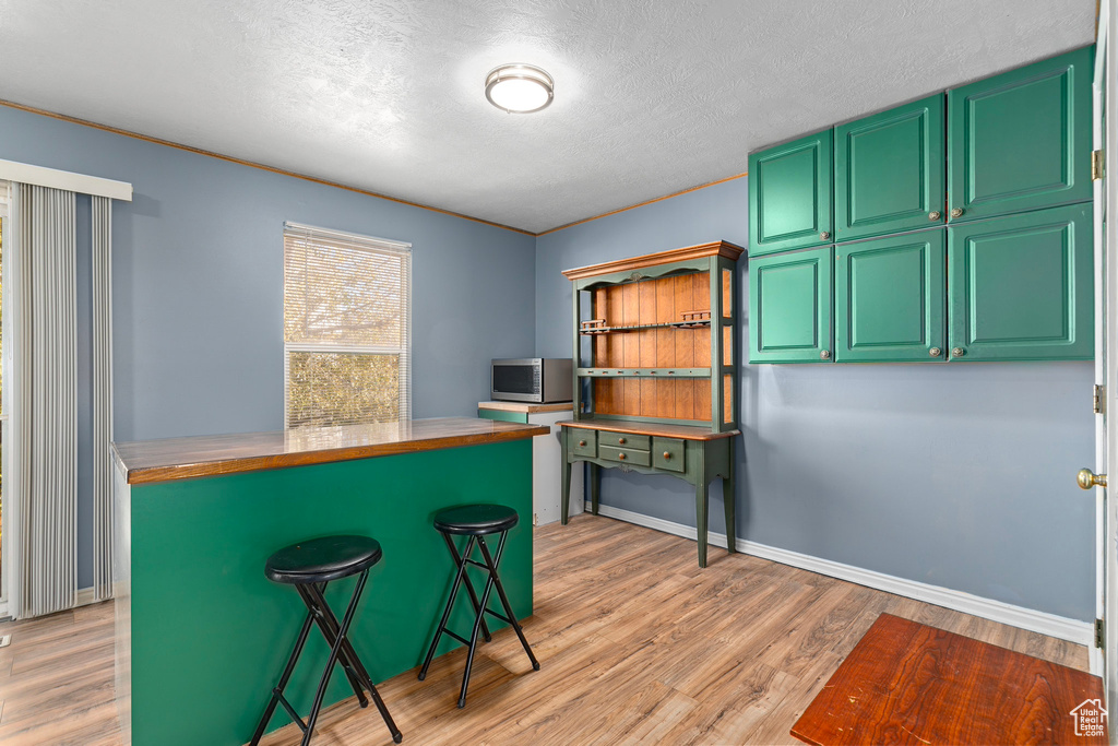 Kitchen with green cabinets, a textured ceiling, butcher block countertops, a breakfast bar, and light wood-type flooring