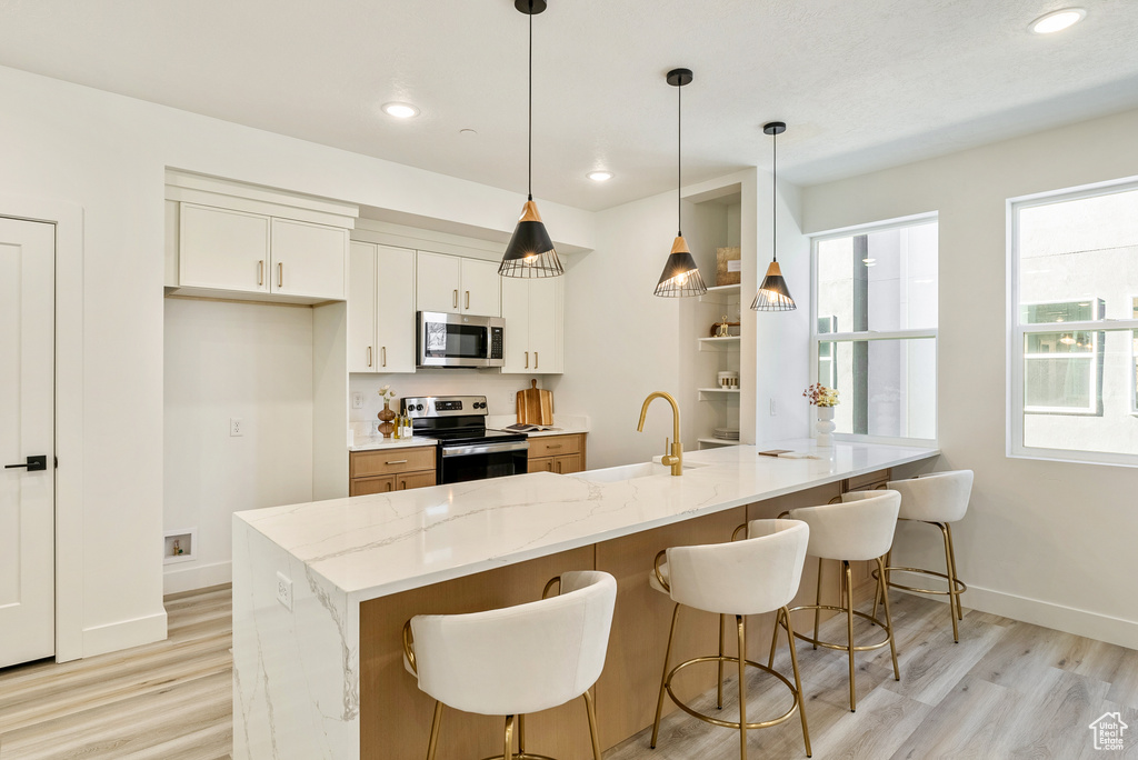 Kitchen featuring appliances with stainless steel finishes, white cabinetry, sink, hanging light fixtures, and light stone counters