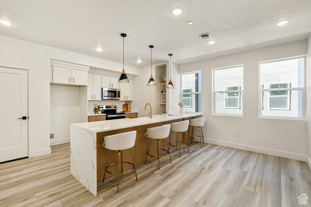 Kitchen with stainless steel appliances, light stone counters, light hardwood / wood-style floors, white cabinets, and decorative light fixtures