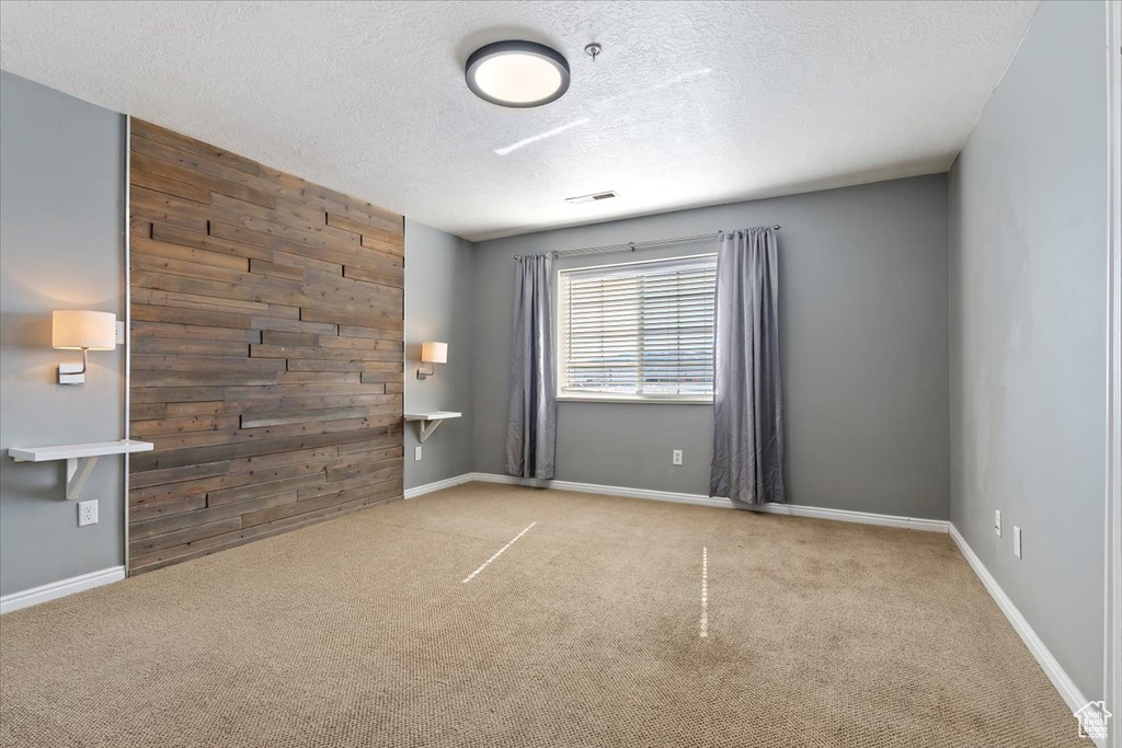 Unfurnished room with an accent wall, light carpet, wooden walls, a textured ceiling, and baseboards