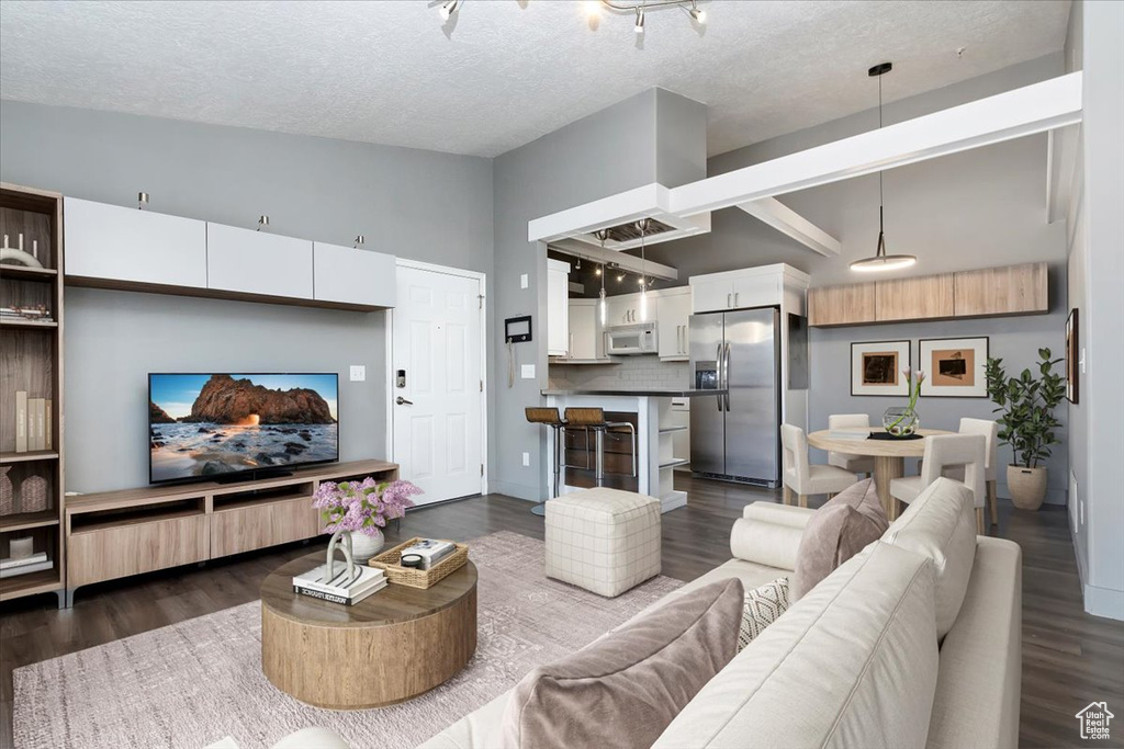 Living area with a textured ceiling, high vaulted ceiling, dark wood-style flooring, and baseboards