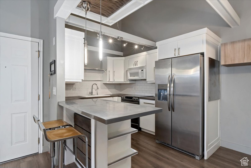 Kitchen with dark wood-style flooring, a breakfast bar area, appliances with stainless steel finishes, white cabinetry, and a sink