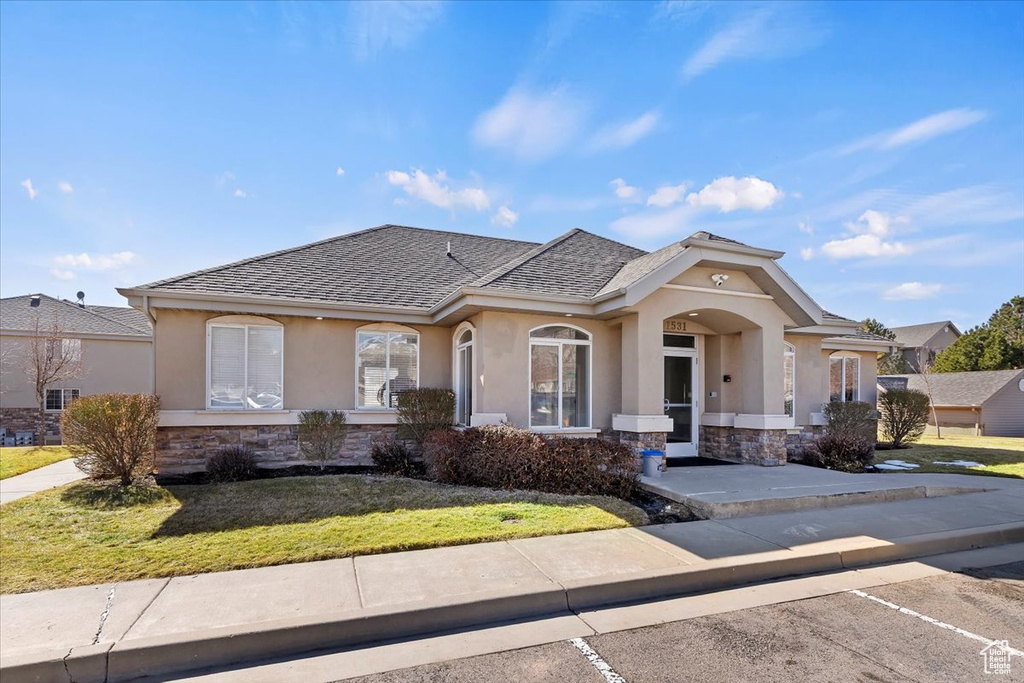 View of front facade featuring stone siding, a shingled roof, a front lawn, and stucco siding