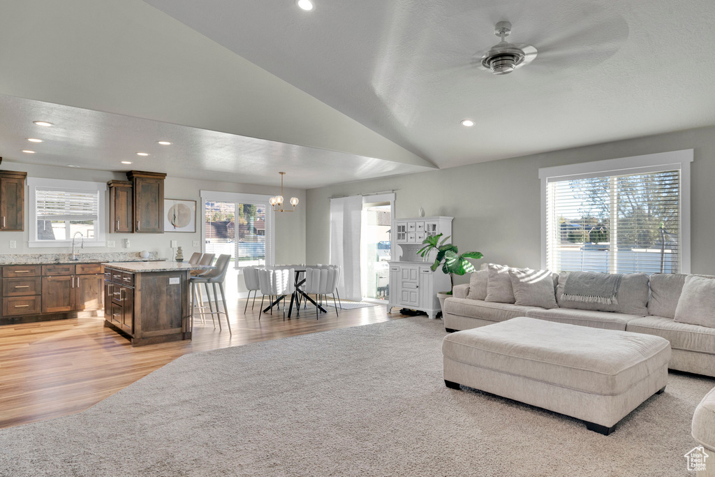 Living room featuring ceiling fan with notable chandelier, a healthy amount of sunlight, light wood-type flooring, and vaulted ceiling