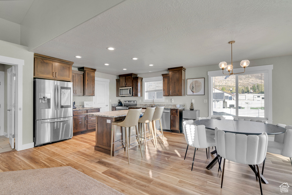 Kitchen with hanging light fixtures, a kitchen island, light wood-type flooring, and appliances with stainless steel finishes