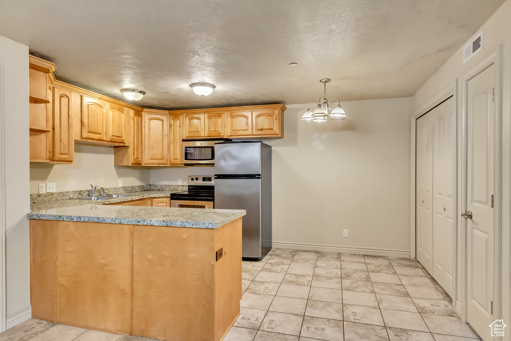 Kitchen with stainless steel appliances, kitchen peninsula, light brown cabinets, an inviting chandelier, and hanging light fixtures