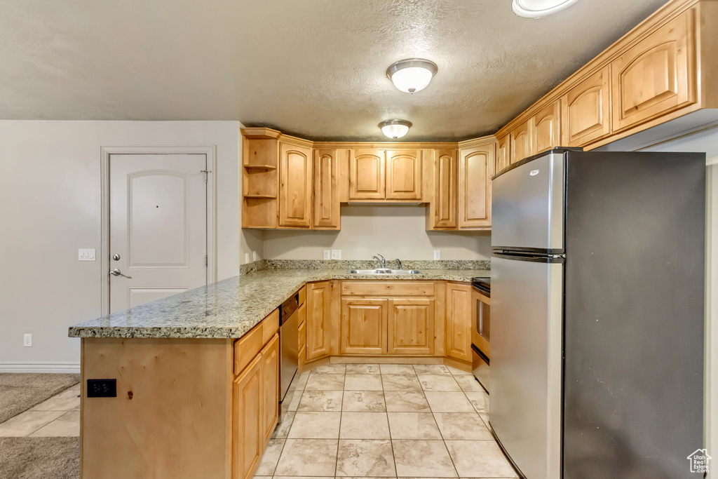 Kitchen with light stone counters, stainless steel appliances, a textured ceiling, light brown cabinetry, and sink