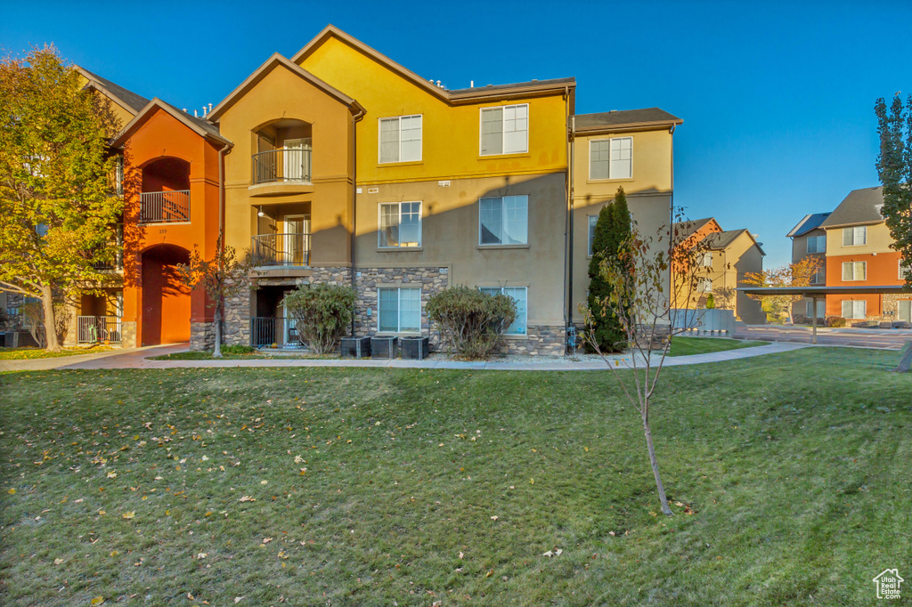 View of front of home featuring central air condition unit, a front yard, and a balcony