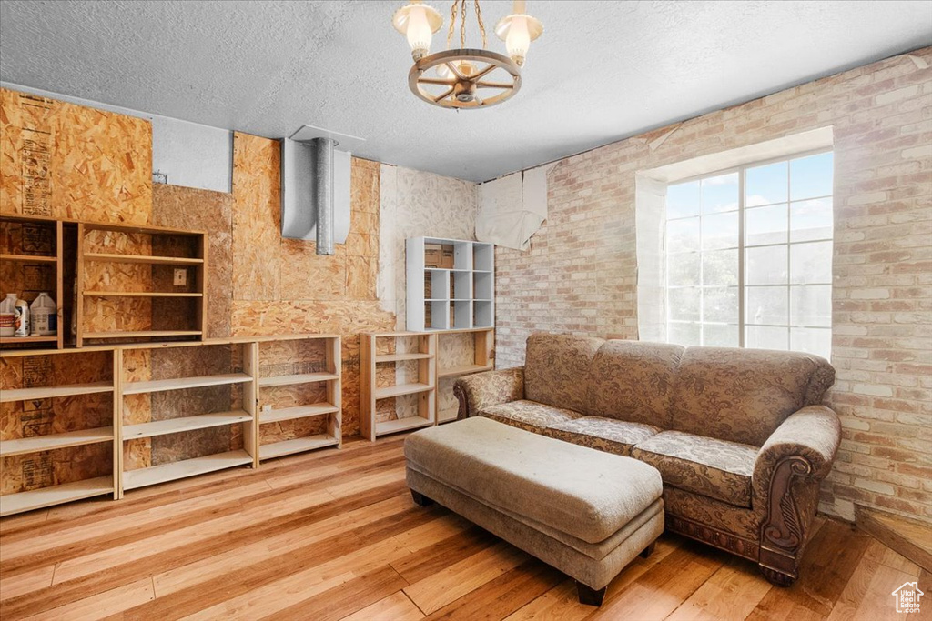 Living area with a textured ceiling, brick wall, light hardwood / wood-style flooring, and a notable chandelier
