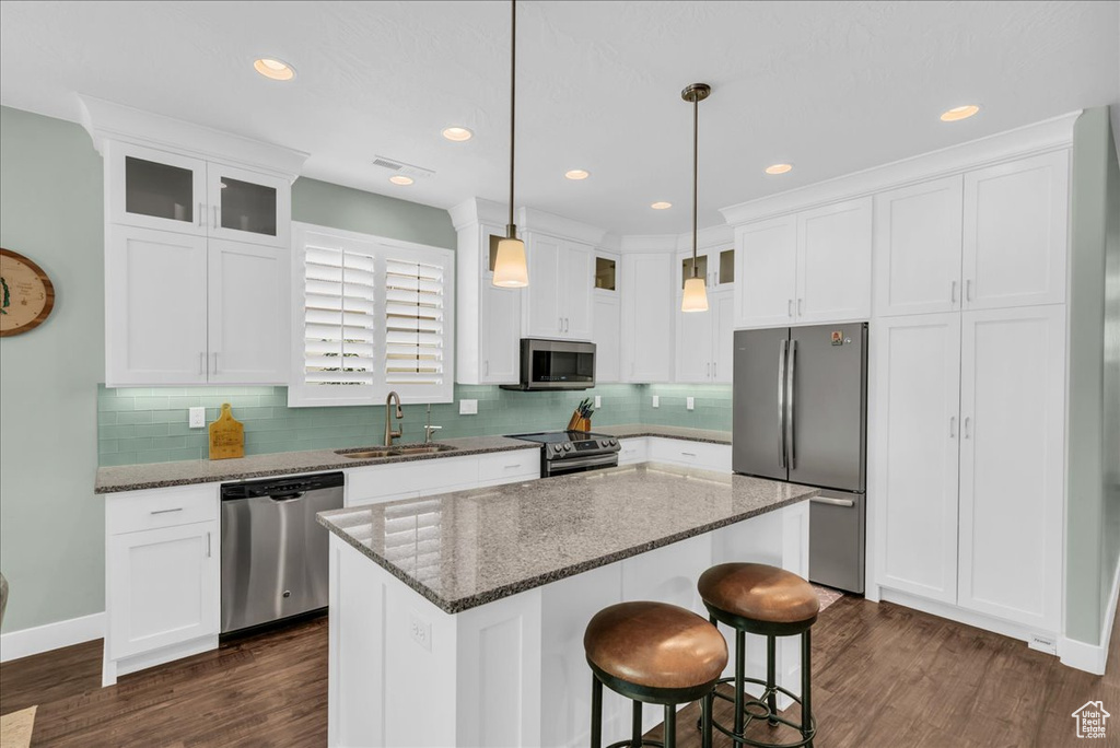 Kitchen featuring sink, a center island, white cabinetry, stainless steel appliances, and dark stone counters