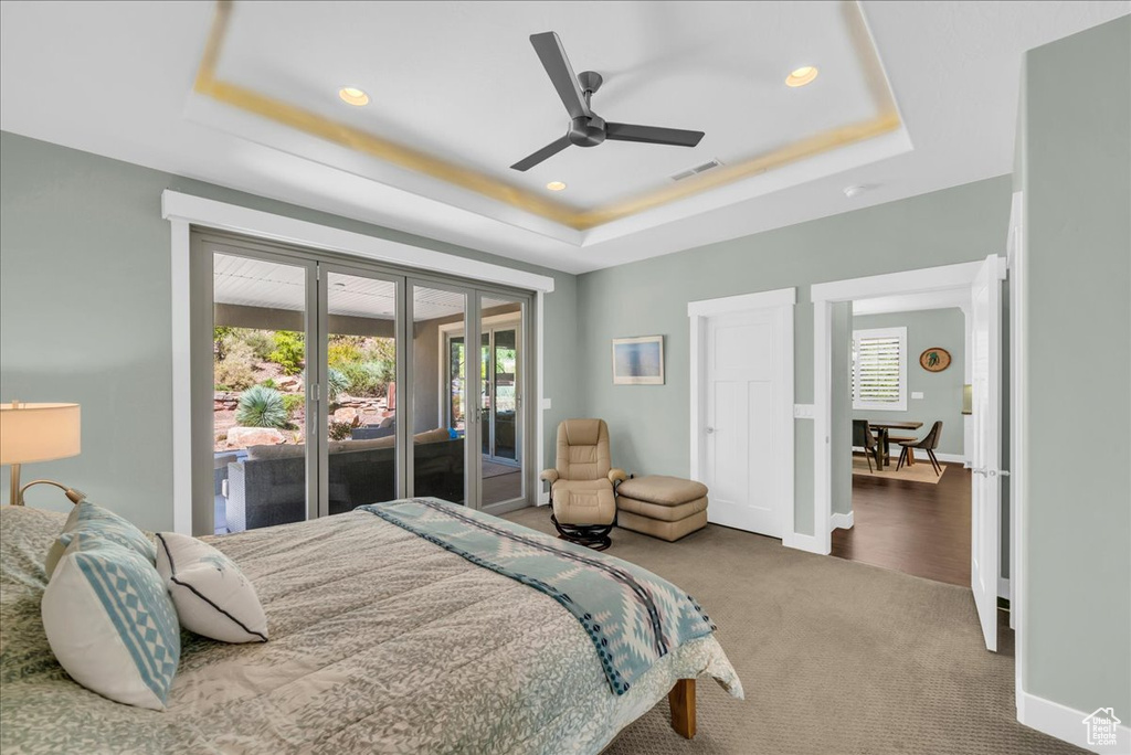 Carpeted bedroom featuring multiple windows, access to exterior, a tray ceiling, and ceiling fan