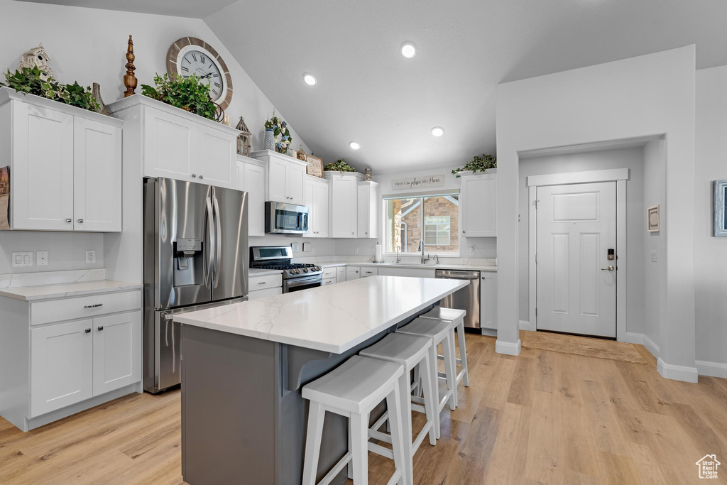 Kitchen with stainless steel appliances, light hardwood / wood-style floors, lofted ceiling, and a center island