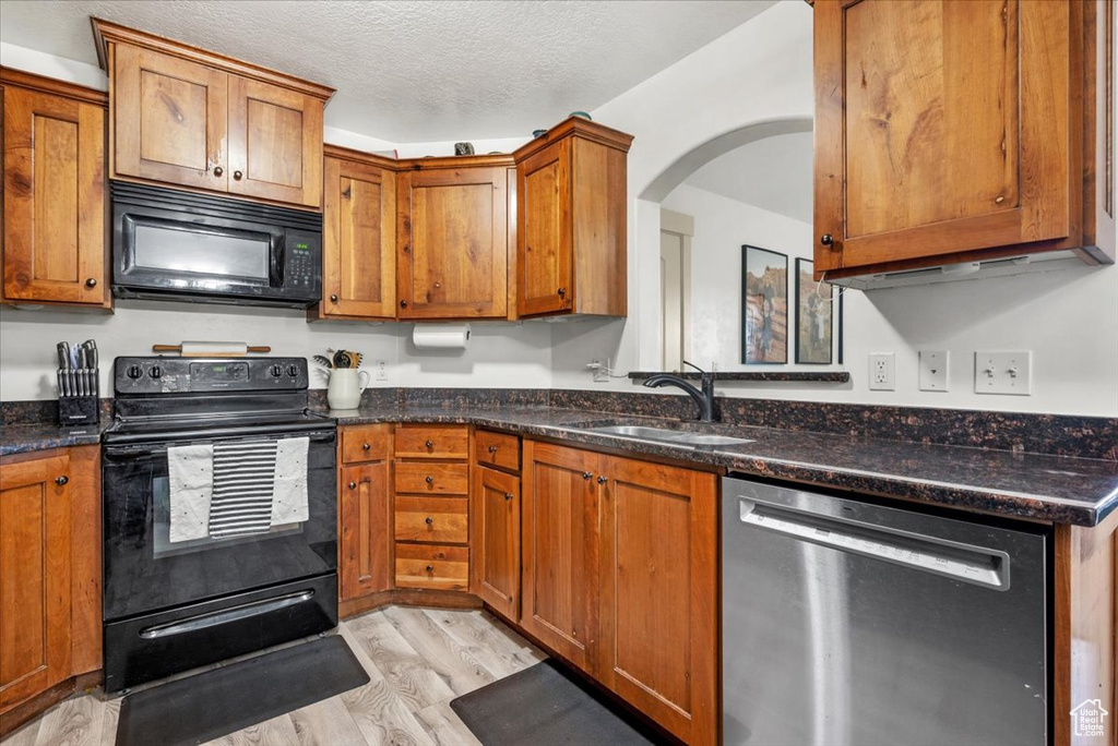 Kitchen featuring black appliances, sink, light hardwood / wood-style floors, and dark stone countertops