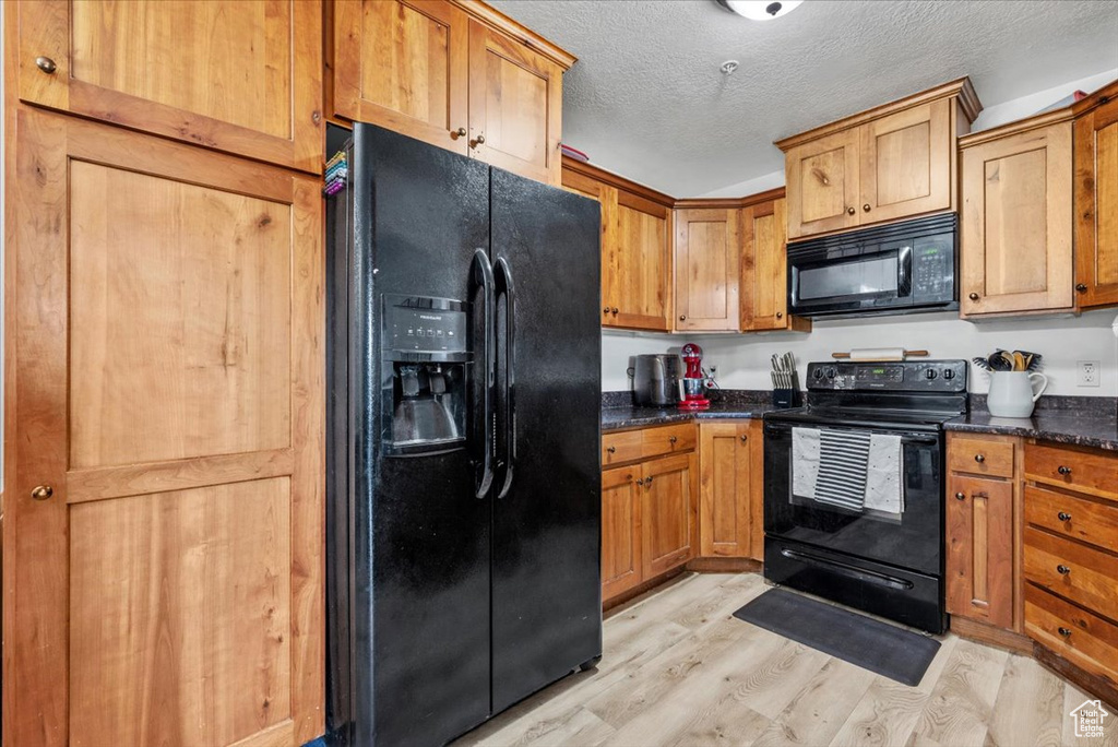 Kitchen featuring light wood-type flooring, dark stone counters, black appliances, and a textured ceiling