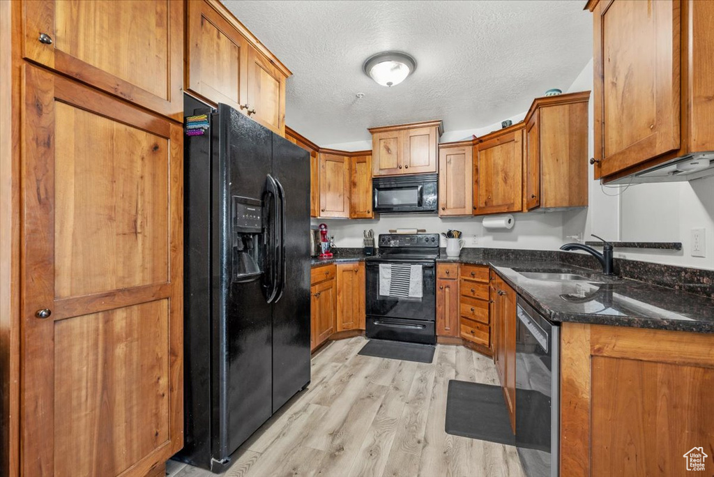 Kitchen with dark stone counters, black appliances, a textured ceiling, sink, and light hardwood / wood-style flooring