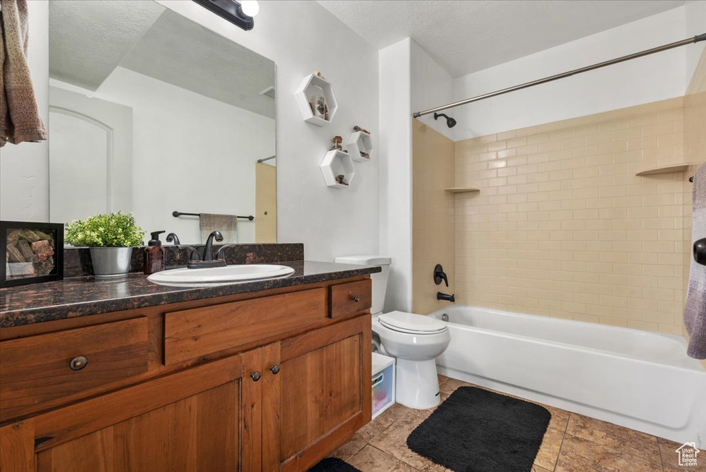 Full bathroom with vanity, toilet, a textured ceiling, and tiled shower / bath combo