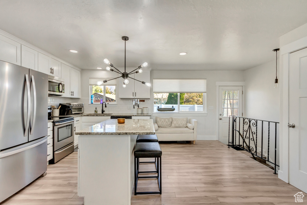 Kitchen with stainless steel appliances, light hardwood / wood-style floors, hanging light fixtures, a kitchen island, and white cabinetry