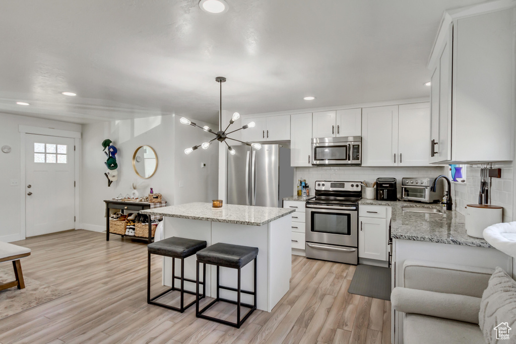 Kitchen featuring stainless steel appliances, light hardwood / wood-style floors, white cabinetry, sink, and a center island