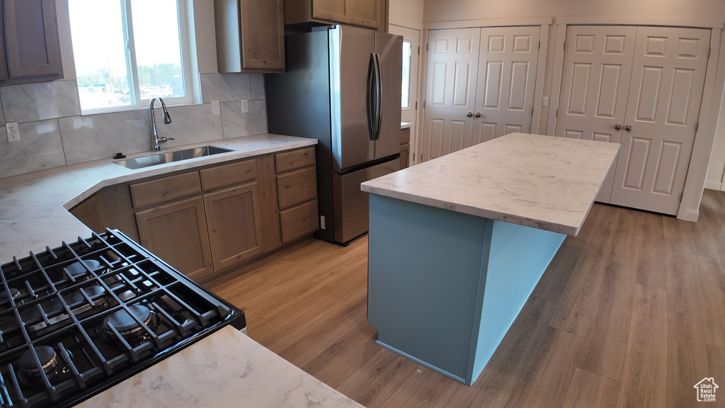 Kitchen featuring stainless steel refrigerator, sink, a kitchen island, black range with gas cooktop, and light wood-type flooring