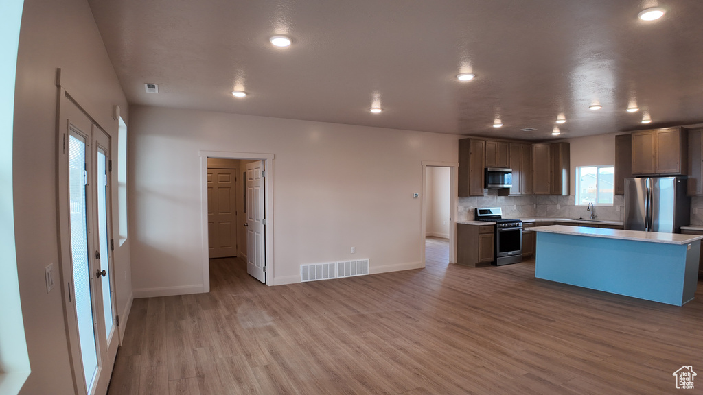 Kitchen with tasteful backsplash, stainless steel appliances, light wood-type flooring, sink, and a center island