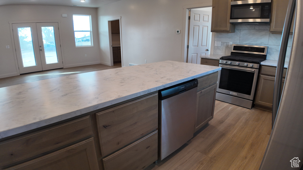 Kitchen featuring light wood-type flooring, french doors, backsplash, and stainless steel appliances