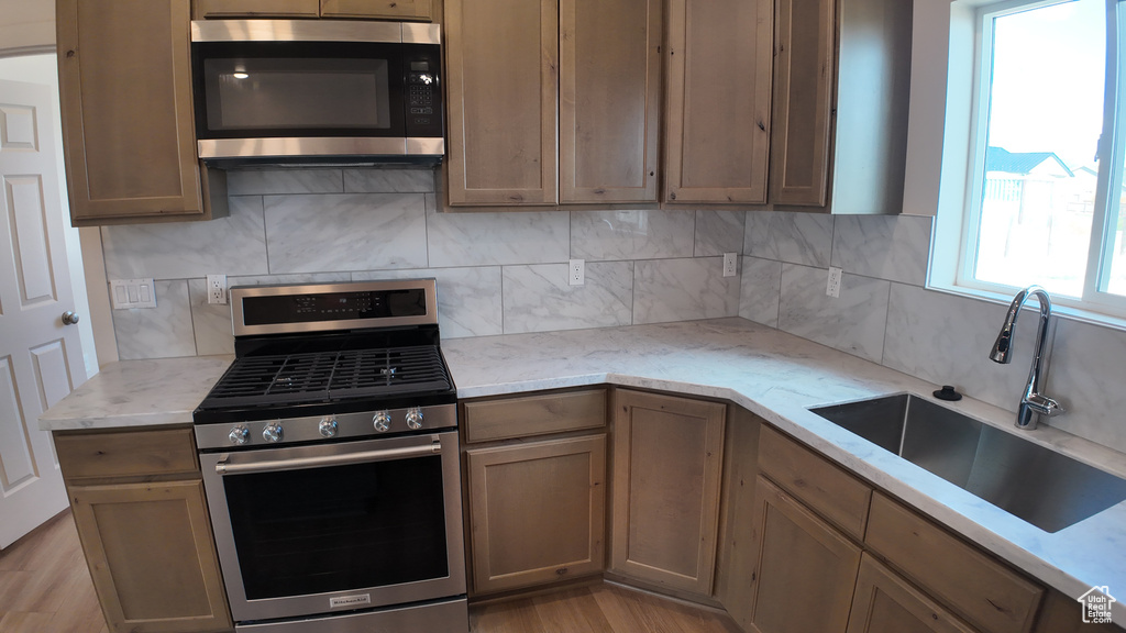 Kitchen with sink, light hardwood / wood-style flooring, appliances with stainless steel finishes, and tasteful backsplash