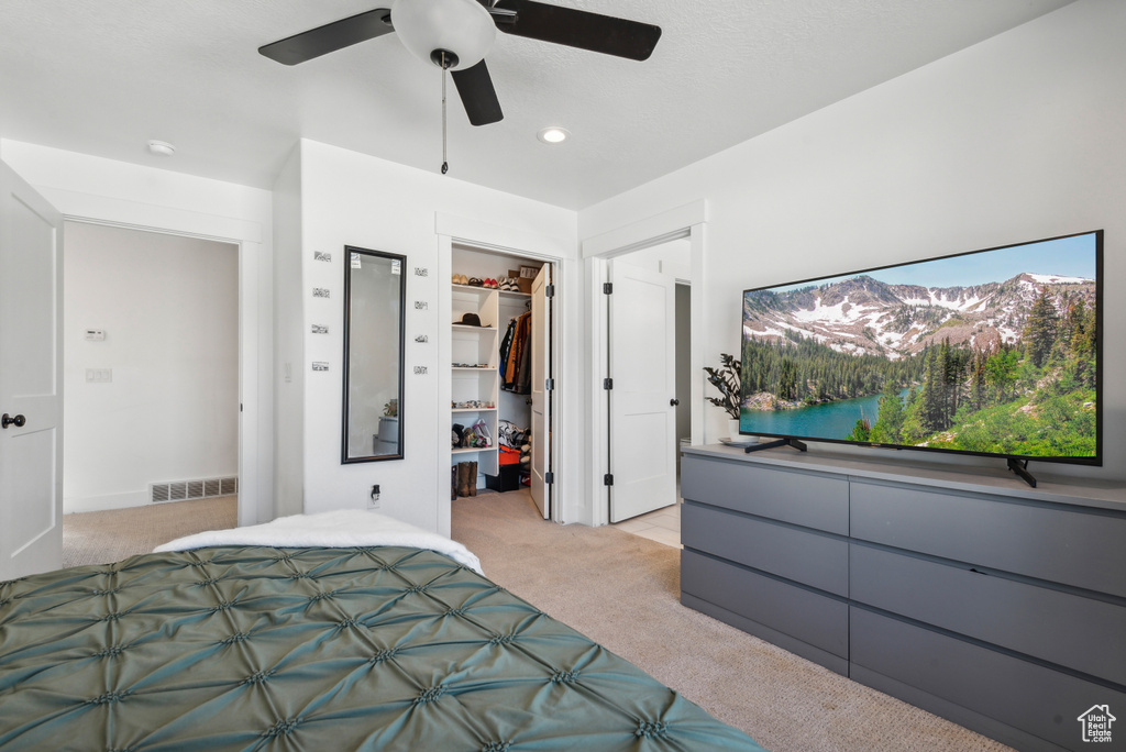 Bedroom with light colored carpet, ceiling fan, a walk in closet, and a closet