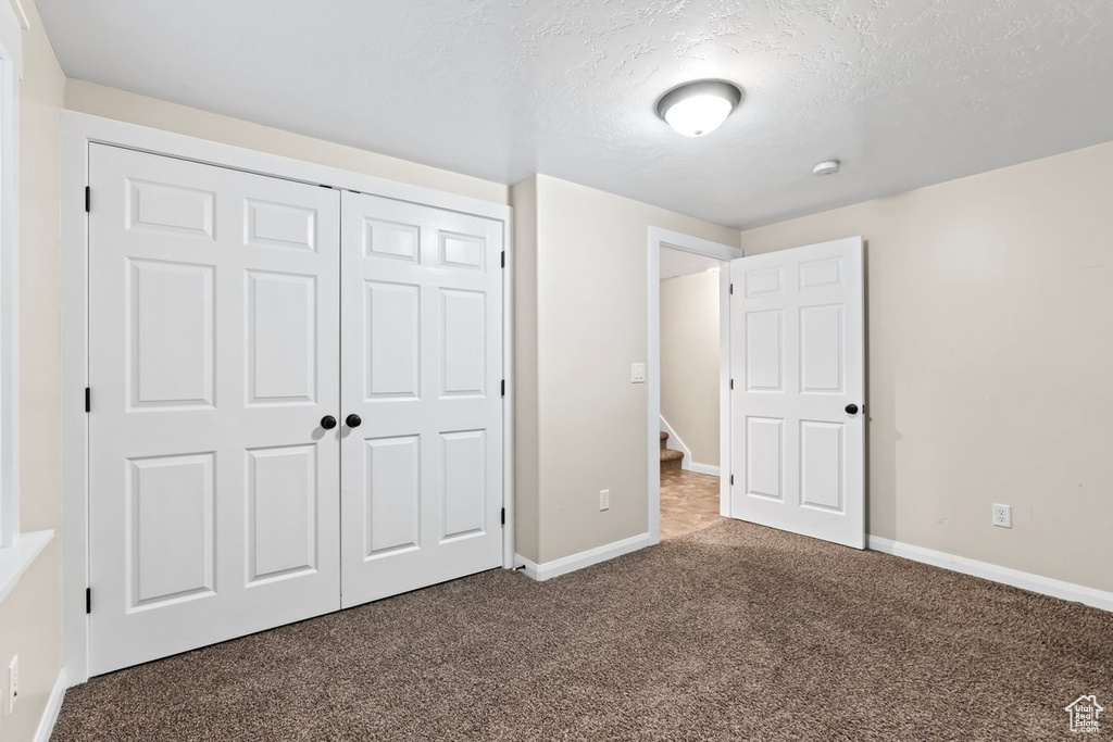 Unfurnished bedroom featuring carpet flooring, a textured ceiling, and a closet