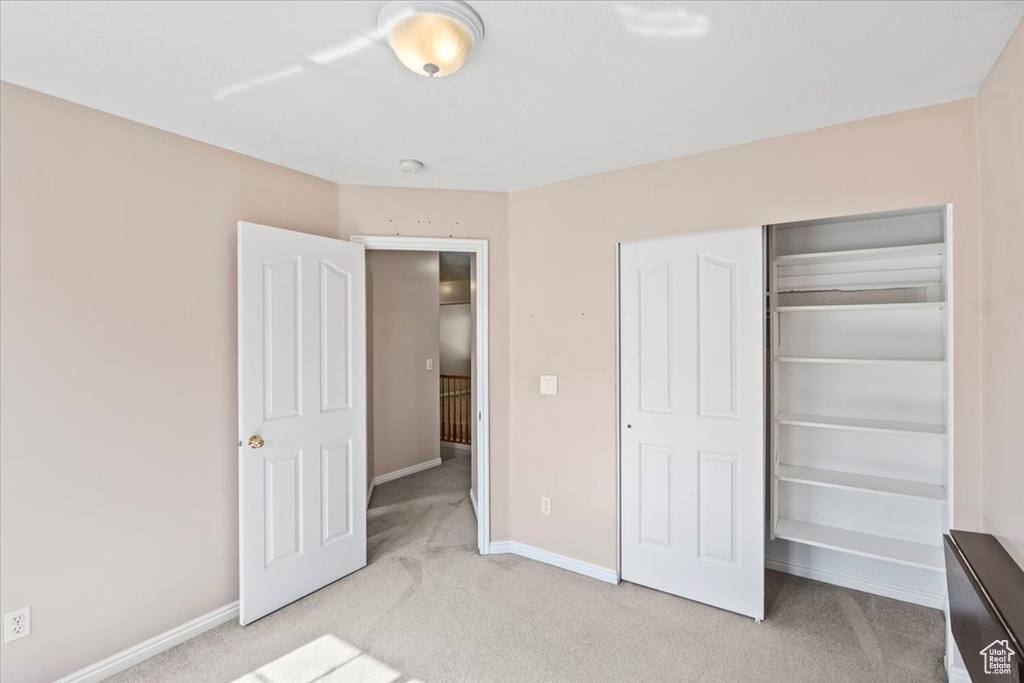 Unfurnished bedroom featuring light carpet, baseboards, and a closet