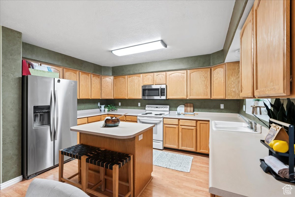 Kitchen featuring appliances with stainless steel finishes, a kitchen bar, light hardwood / wood-style flooring, sink, and a center island