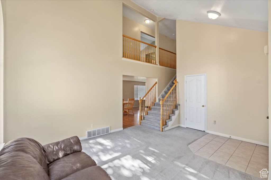 Tiled living area with stairway, baseboards, carpet floors, and a high ceiling
