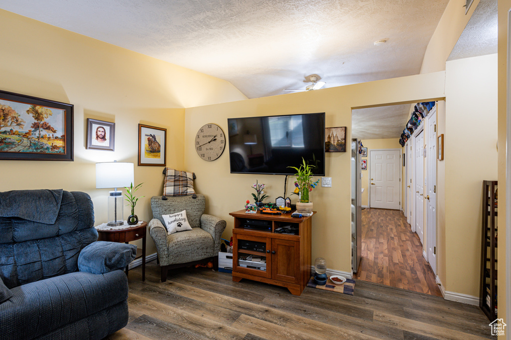 Living room featuring dark hardwood / wood-style flooring, lofted ceiling, a textured ceiling, and ceiling fan