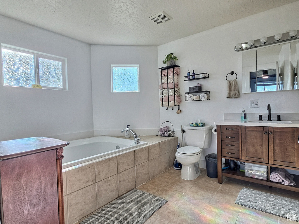 Bathroom featuring tile patterned floors, vanity, a textured ceiling, tiled tub, and toilet