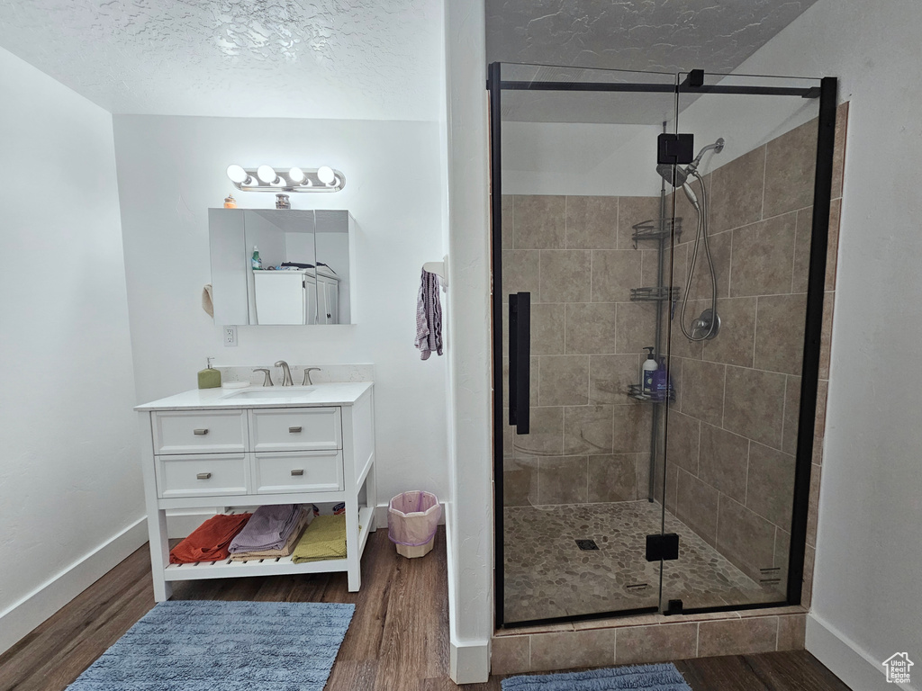 Bathroom with a textured ceiling, vanity, wood-type flooring, and a shower with shower door