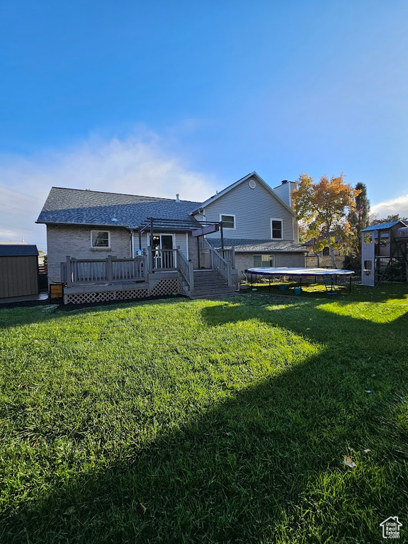 Rear view of property with a wooden deck, a yard, and a trampoline