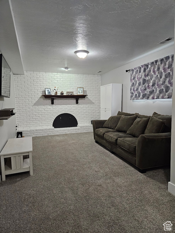 Living room featuring a brick fireplace, dark colored carpet, brick wall, and a textured ceiling