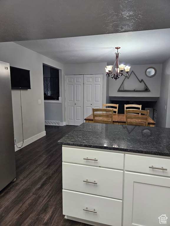 Kitchen with dark hardwood / wood-style floors, dark stone countertops, an inviting chandelier, hanging light fixtures, and white cabinets